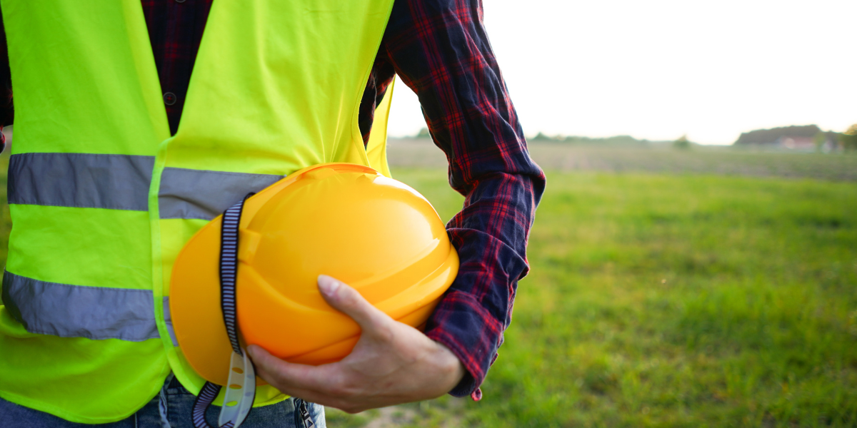 A construction worker holding a yellow safety helmet and wearing a high visibility vest